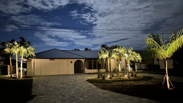 Ein Haus mit gepflasterter Auffahrt, Garage und Palmen.