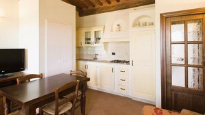 Une cuisine avec des meubles blancs, une table à manger en bois et un téléviseur.