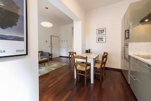 Une cuisine moderne avec un coin repas, des chaises en bois, une table blanche et un luminaire suspendu.