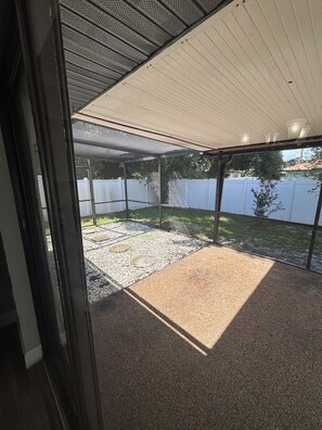 An enclosed patio area with a gravel floor and a white fence in the background.