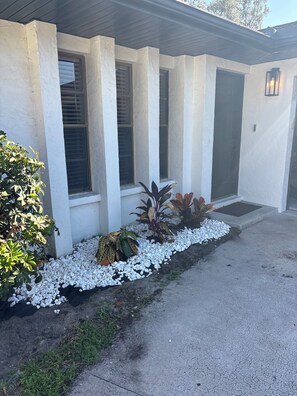 A house with a white exterior, a front door, and a small garden with white pebbles and various plants.