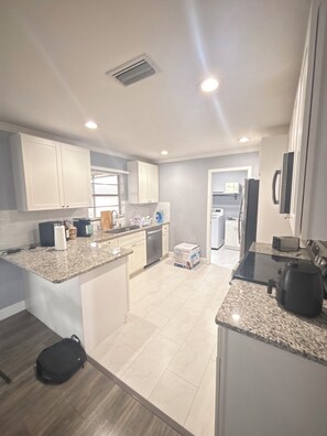 A modern kitchen with granite countertops, white cabinetry, and a built-in dishwasher.