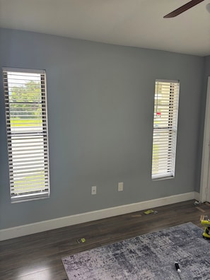 A room with two windows, a ceiling fan, and a patterned rug on the floor.