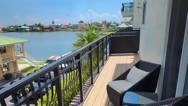 A balcony with wicker furniture, a view of a lake, and a building with a balcony railing. - Memories Await, Garber Getaways! Waterfront retreat, 100 steps to private beach! (Naples)