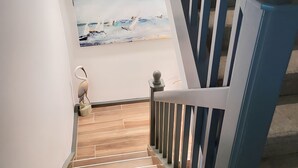 A wooden staircase with a blue railing leading to a landing where a painting of a beach scene is displayed. - Memories Await, Garber Getaways! Waterfront retreat, 100 steps to private beach! (Naples)