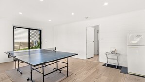 Quarto moderno com mesa de ping pong, uma pequena mesa com uma cesta e um frigorífico.