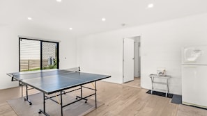 Quarto moderno com mesa de ping pong, uma pequena mesa com uma cesta e um frigorífico.