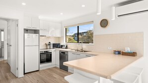 Uma cozinha moderna com armários brancos, forno embutido, micro-ondas e lava-louças, uma janela grande com vista e um relógio na parede.