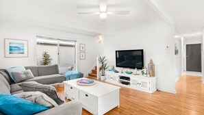 Een moderne woonkamer met een grijze bank, een witte salontafel en een flatscreen televisie op een wit kastje.
