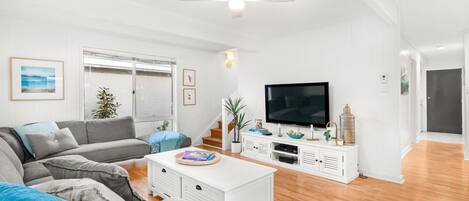 Een moderne woonkamer met een grijze bank, een witte salontafel en een flatscreen televisie op een wit kastje.