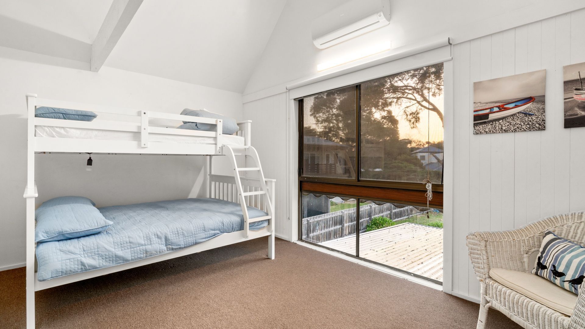A bunk bed room with a view of a wooden deck and a wicker chair.