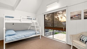 Een slaapkamer met stapelbedden en uitzicht op een houten terras en een rieten stoel.