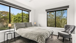 A bedroom with a bed, a chair, a lamp, and large windows with a view of trees. - Anderson Getaway in Cowes (Cowes)