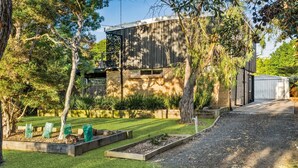 A modern house with a brick exterior, a wooden deck, and a well-maintained garden with raised beds and a lawn. - Anderson Getaway in Cowes (Cowes)