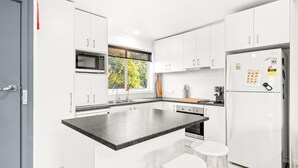 A modern kitchen with white cabinets, a central island, a built-in microwave, a refrigerator, and a window with a view of trees. - Anderson Getaway in Cowes (Cowes)