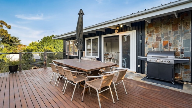 A deck with a wooden table and wicker chairs, a grill, and a stone wall. - Anderson Getaway in Cowes (Cowes)