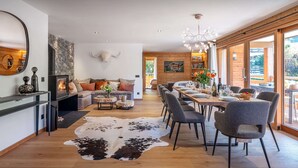 Un soggiorno moderno con camino, un'area pranzo con tavolo e sedie in legno, e un'ampia finestra che offre vista sull'esterno.