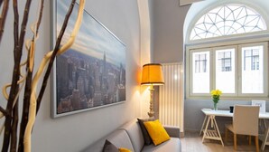 A modern living room with a grey sofa, yellow cushions, a cityscape painting, a lamp, a dining table with chairs, and a window with a view. - GuestHost - Consolata Square Elegant Loft x4 (Torino)