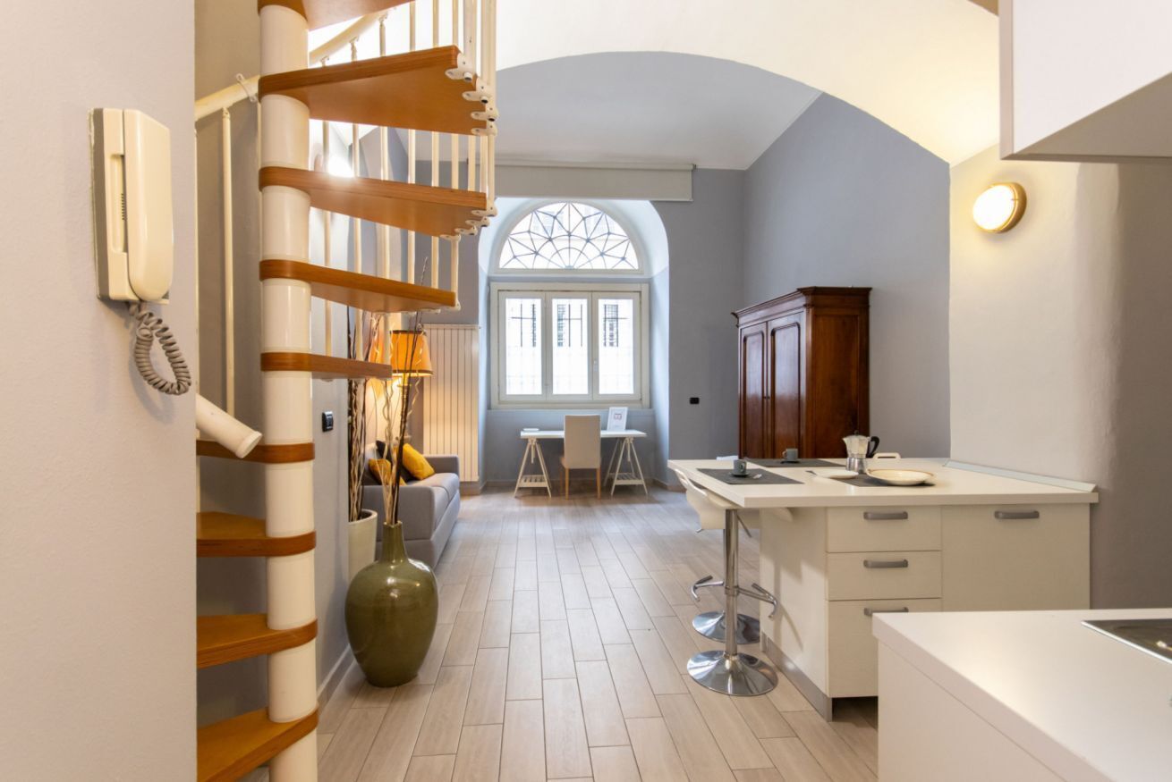 A modern kitchen with a central island, a staircase, and a dining area with a view through a window.