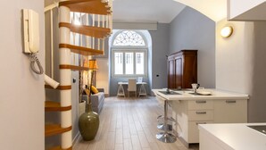 A modern kitchen with a central island, a staircase, and a dining area with a view through a window. - GuestHost - Consolata Square Elegant Loft x4 (Torino)