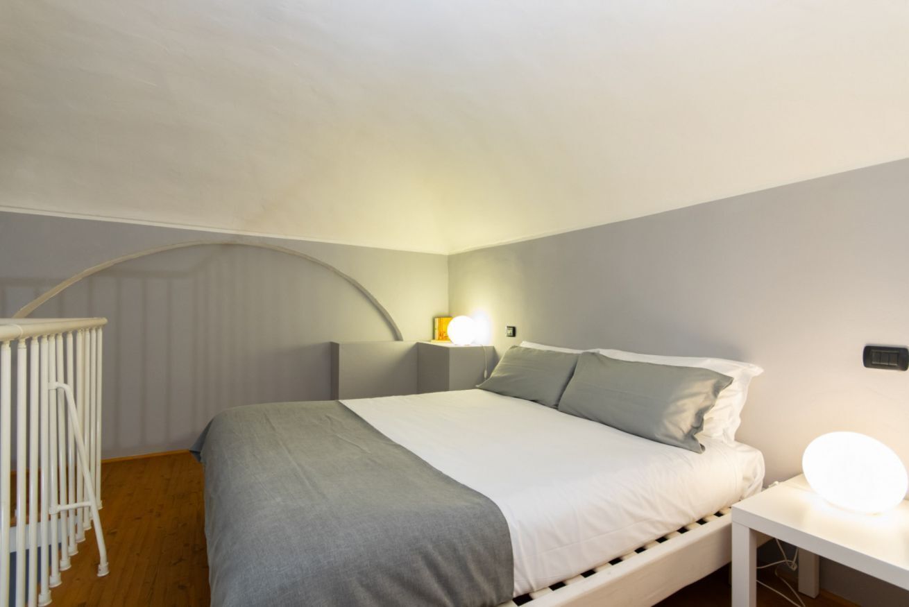A bedroom with a bed, bedside table, lamp, and a crib.