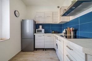 A modern kitchen with a stainless steel refrigerator, a microwave, a washing machine, and a sink.