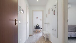 Ein Korridor mit einer Holztür, einer Bank, einem Schreibtisch mit Stuhl und einem Bett im Hintergrund.