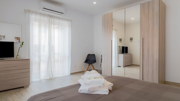 Ein modernes Schlafzimmer mit Bett, Fernseher, Kleiderschrank und Stuhl.