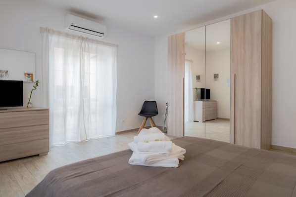 A modern bedroom with a bed, a TV, a wardrobe, and a chair.