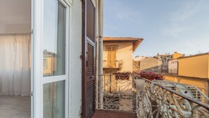 Ein Balkon mit Metallgeländer, einer Schiebeglastür und Blick auf benachbarte Gebäude.