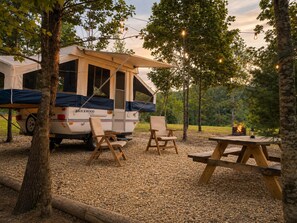 A campervan with a canopy, two chairs, a picnic table, and a campfire.