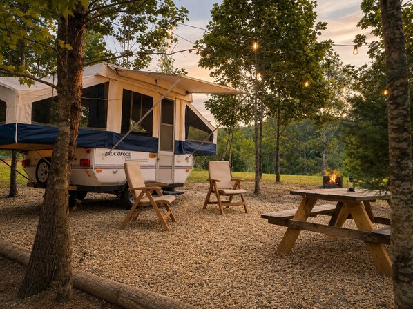 Un camping-car équipé d’un auvent, de deux chaises, d’une table de pique-nique et d’un foyer de camp.