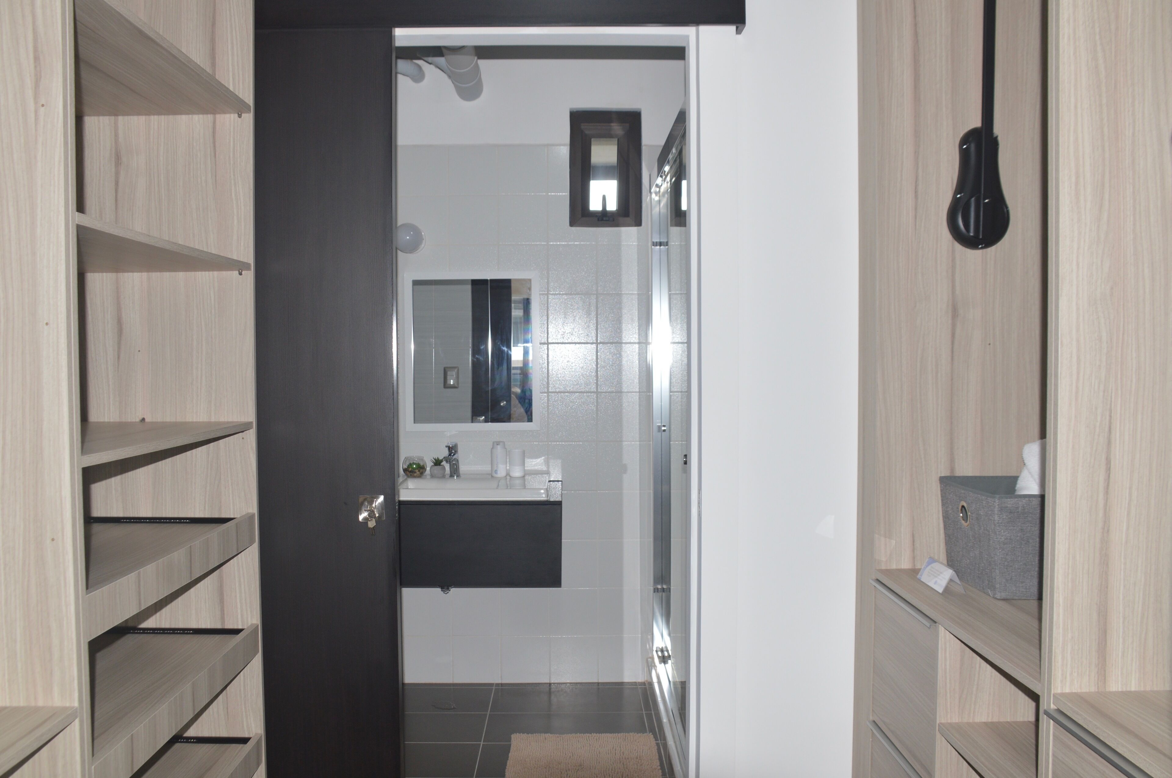Un baño moderno con una puerta oscura, baldosas blancas, un espejo y un perchero.