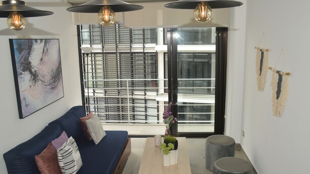 A modern living room with a blue sofa, a wooden coffee table with plants, and a large window with blinds.