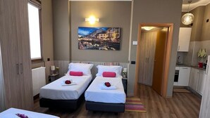A hotel room with two beds, a painting of a cityscape, a kitchenette, and a bathroom. - Bnbook TommasoGrossi Studio (Rho)