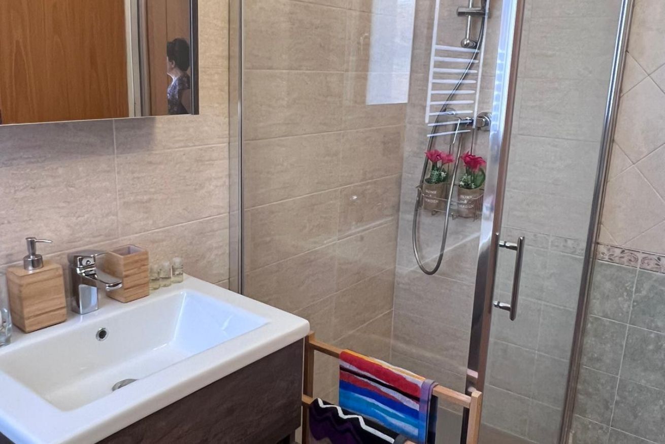 A bathroom with a white sink, wooden soap dispensers, a towel rack with a colorful towel, and a shower area with a glass door.