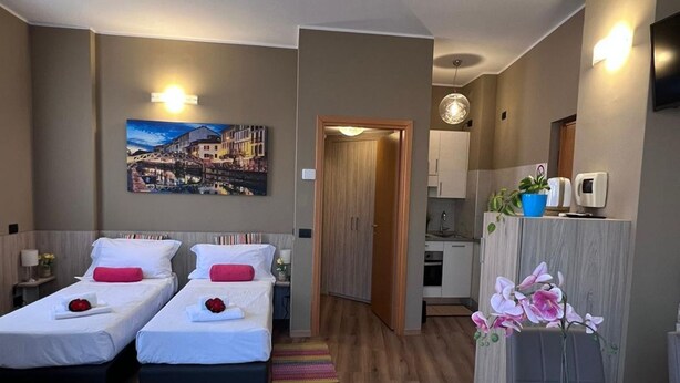 A hotel room with two beds, a painting of a cityscape, a kitchenette, and a bathroom visible through an open door. - Bnbook TommasoGrossi Studio (Rho)
