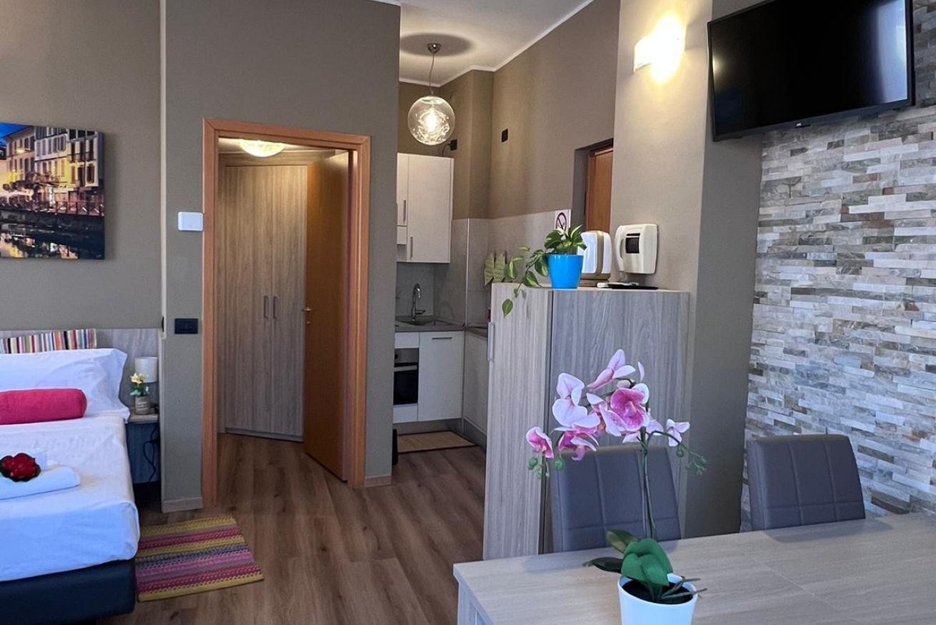 A modern hotel room with a bed, a small desk, a dining area, and a kitchen.