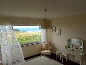 Ein Schlafzimmer mit Blick auf ein Feld und das Meer, ein Stuhl, ein kleiner Tisch und eine Kommode mit Spiegel.