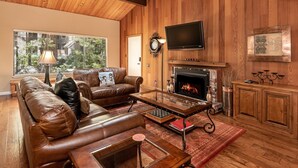 Ein gemütliches Wohnzimmer mit Ledersofa, Couchtisch, Kamin und einem darüber montierten Fernseher.