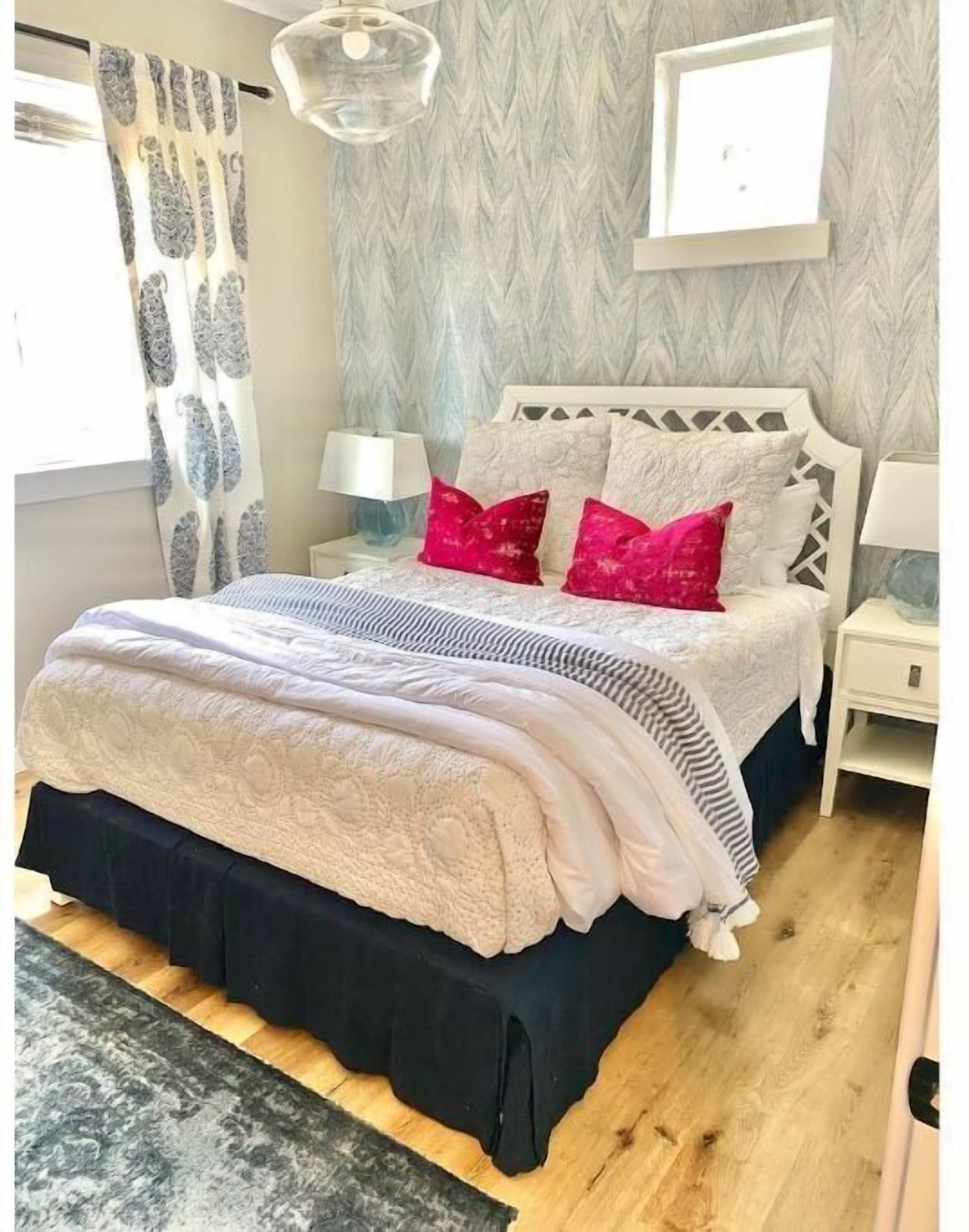 A bedroom with a bed, nightstands, a lamp, a window with curtains, and a wall with a textured pattern.
