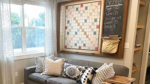 A living room with a grey sofa, a brown leather couch, and a large board game. There is a chalkboard with scores on the wall. - Birdie's: A New 2b in Downtown Hillsboro (Hillsboro)