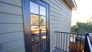 A wooden door with a glass panel, a balcony with a black railing, and a view of a backyard with a wooden fence and trees. - The Isabella Lofthouse on Colorado-Walk to Main

 (Buena Vista)