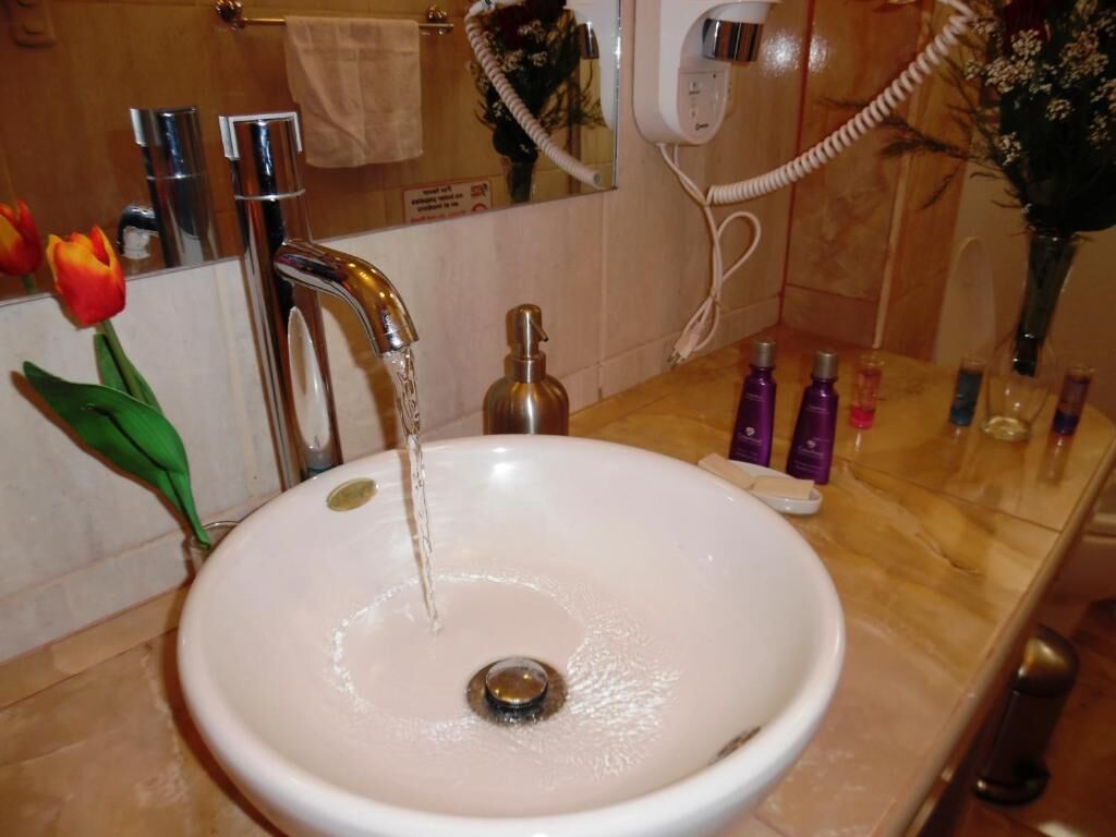 Un baño con lavamanos blanco, espejo, secador de pelo y artículos de aseo en la encimera.