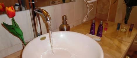 Un baño con lavamanos blanco, espejo, secador de pelo y artículos de aseo en la encimera.