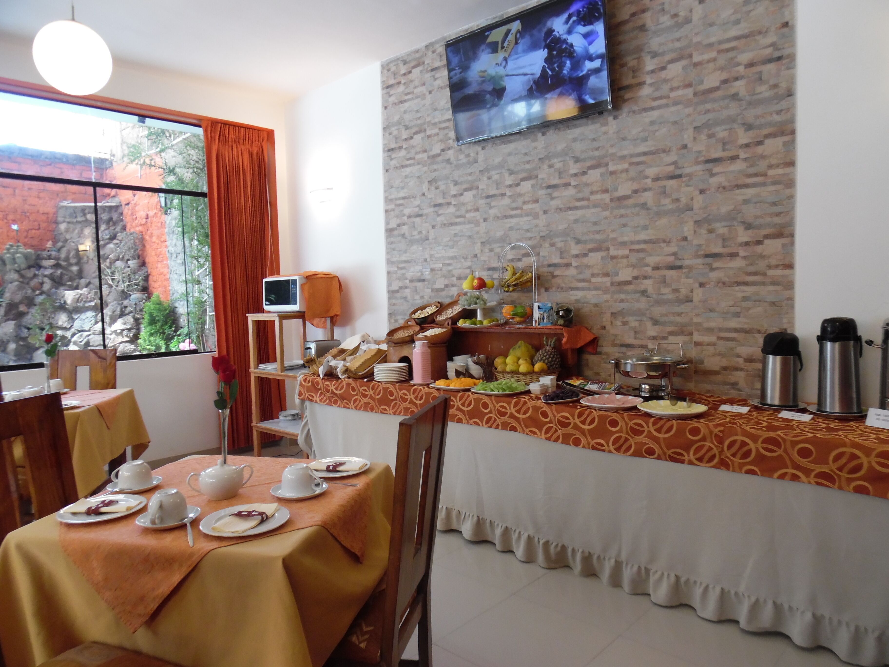 A dining area with a buffet setup, a television mounted on the wall, and a view of a rocky garden through the window.