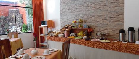 Un espace repas avec un buffet, un téléviseur fixé au mur et une vue sur un jardin rocheux par la fenêtre.