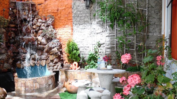A garden with a stone fountain, a small table with a cup and saucer, and a variety of plants and flowers. - HOTEL PUNO TERRA (Puno)