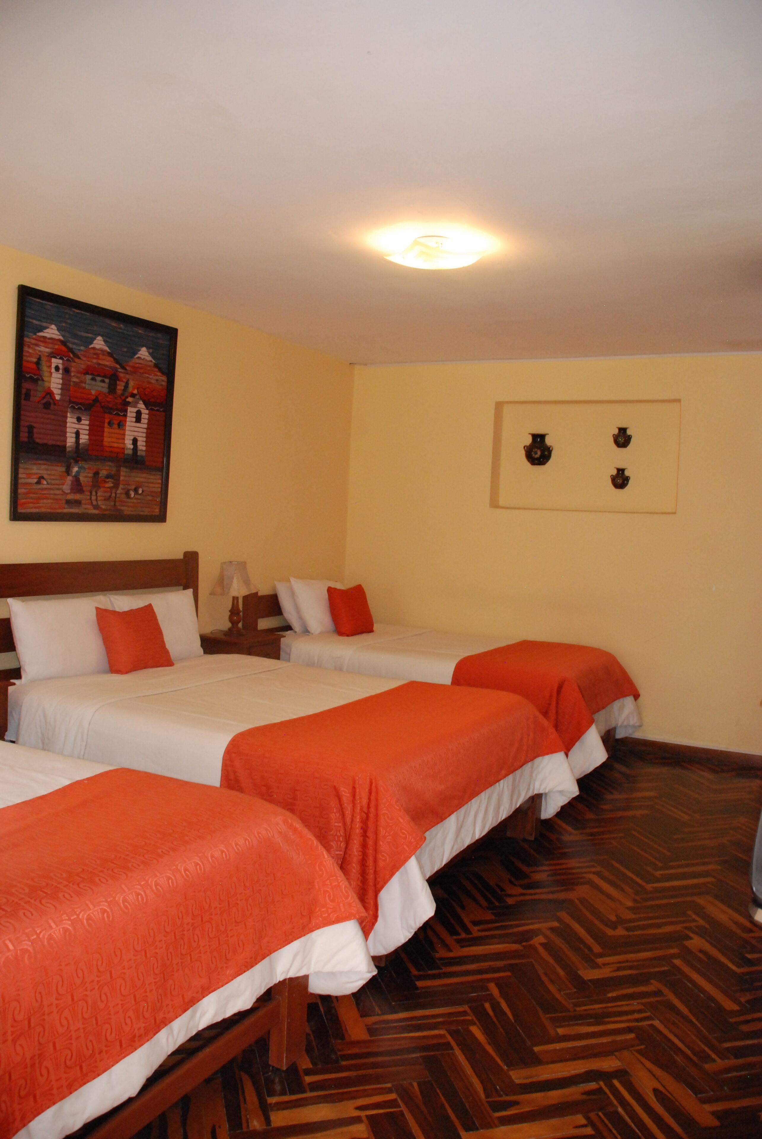 A hotel room with three beds, wooden flooring, a painting on the wall, and a ceiling light.