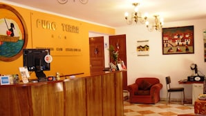A reception area with a wooden counter, a chair, a table, and a painting on the wall. - HOTEL PUNO TERRA (Puno)